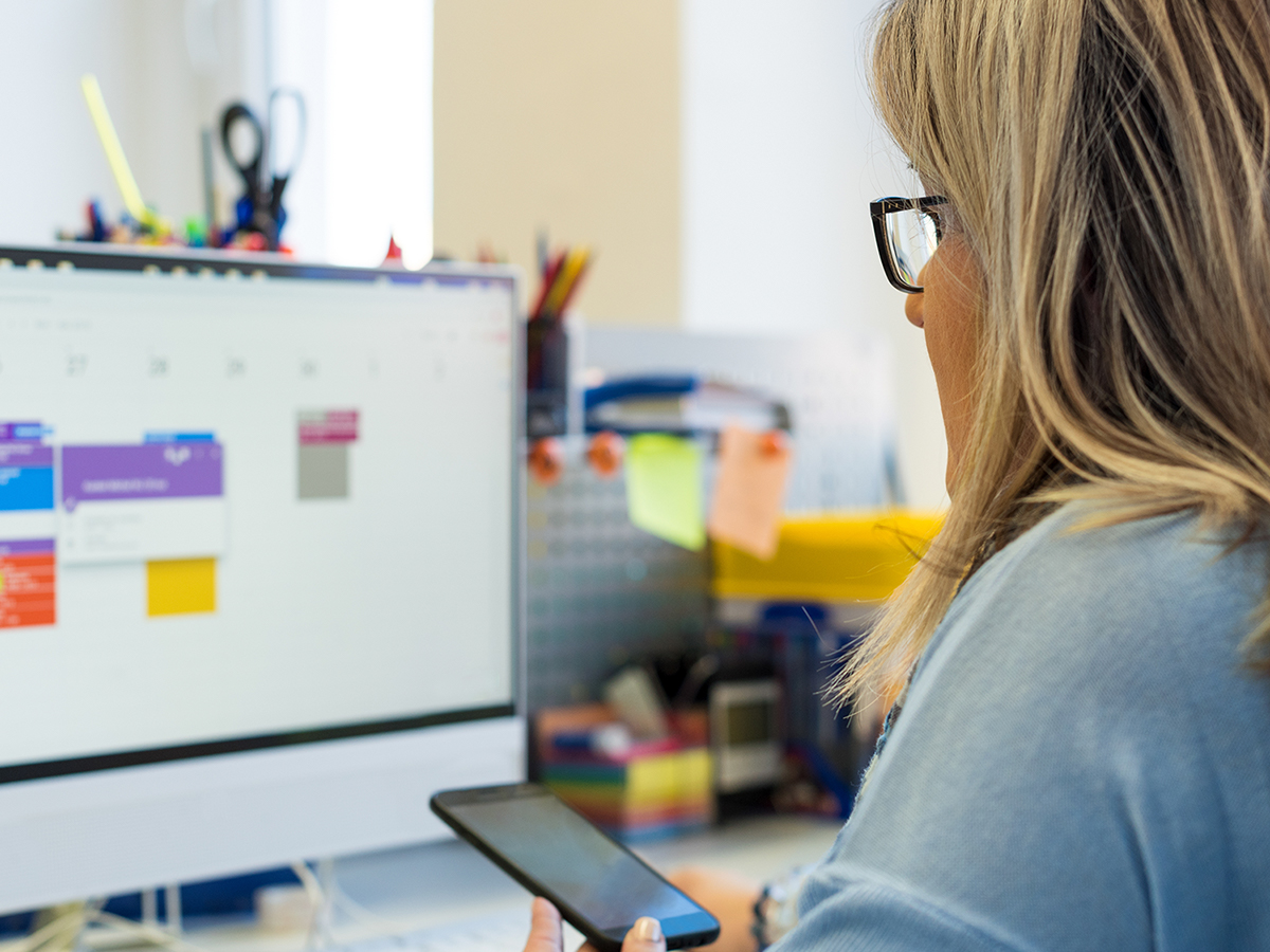 woman looking at phone in front of work computer