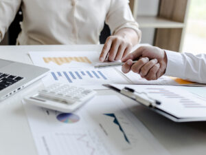 Two businessmen comparing numbers on paperwork with a laptop.