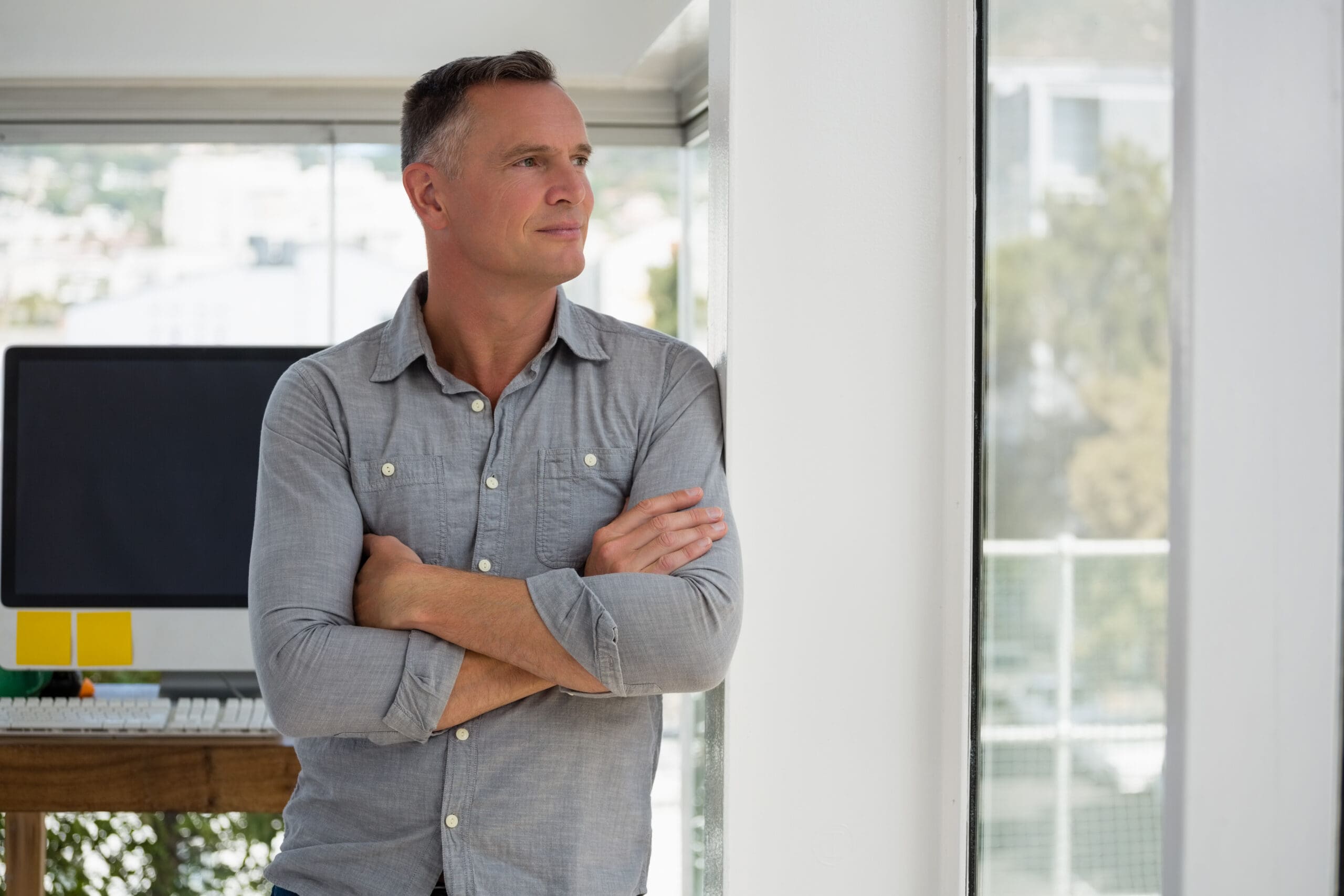 Confident,Businessman,Looking,Through,Window,While,Leaning,On,Wall,At